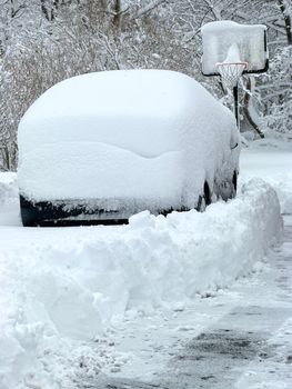 Heavily snow-covered car near a basketball hoop in a winter landscape.